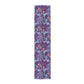 A multicolored table runner with a floral William Morris & Co pattern in pink and green on a blue background, displayed on a table with dishes and cutlery.