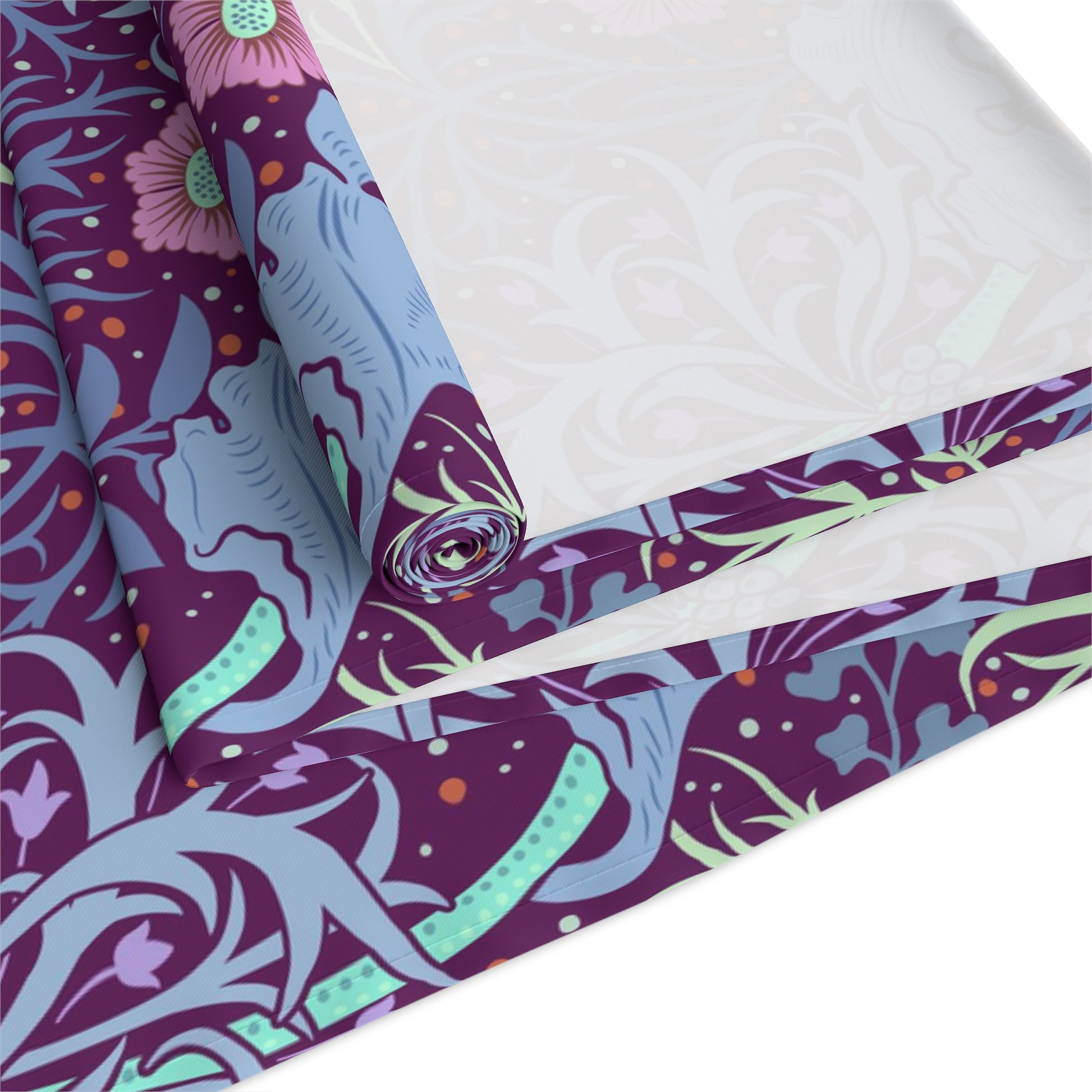 A multicolored table runner with a floral William Morris & Co pattern in pink and green on a blue background, displayed on a table with dishes and cutlery.