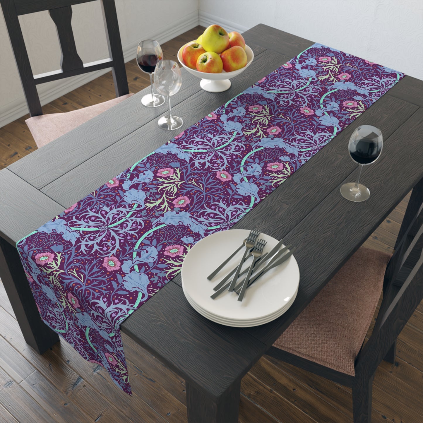 A multicolored table runner with a floral William Morris & Co pattern in pink and green on a blue background, displayed on a table with dishes and cutlery.