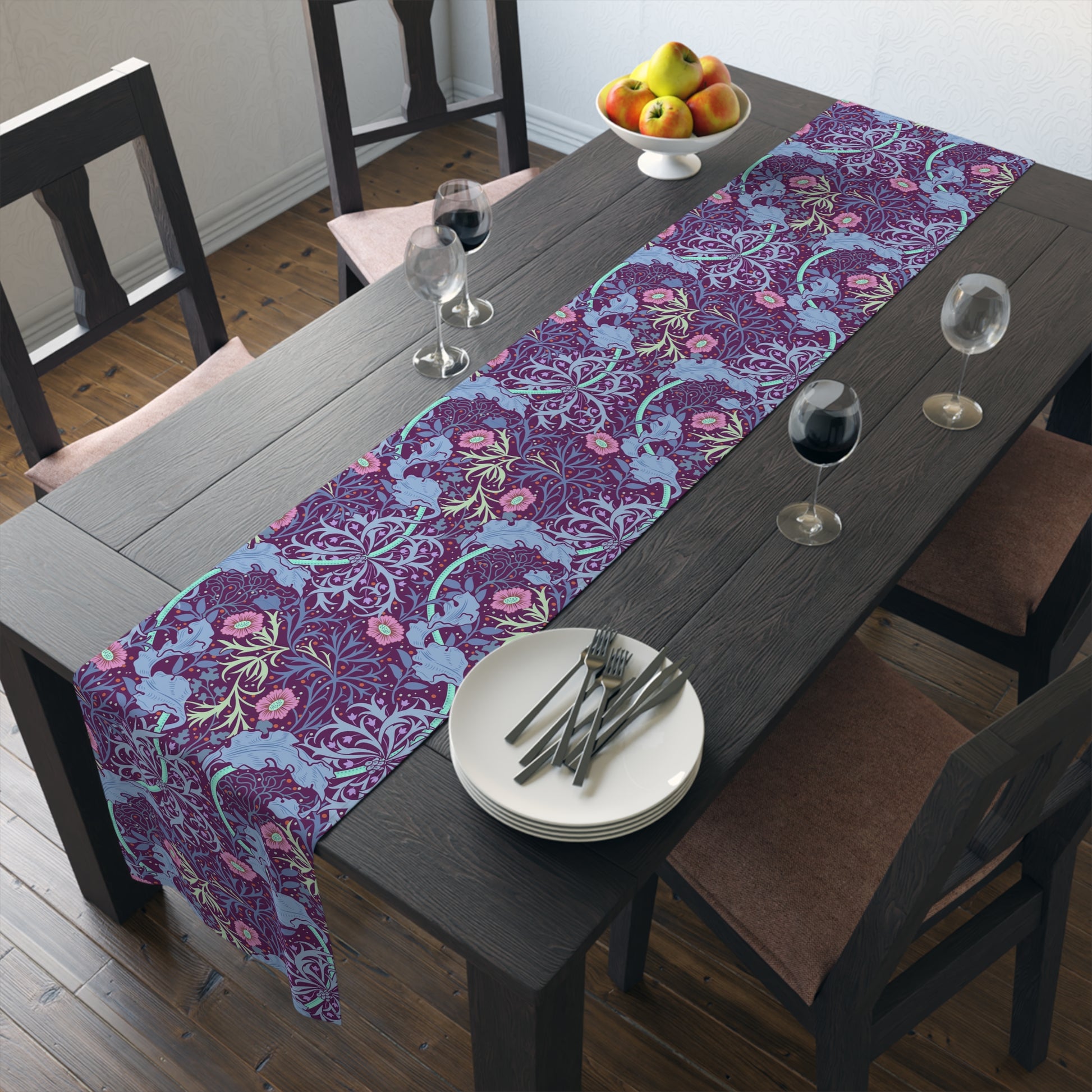A multicolored table runner with a floral William Morris & Co pattern in pink and green on a blue background, displayed on a table with dishes and cutlery.