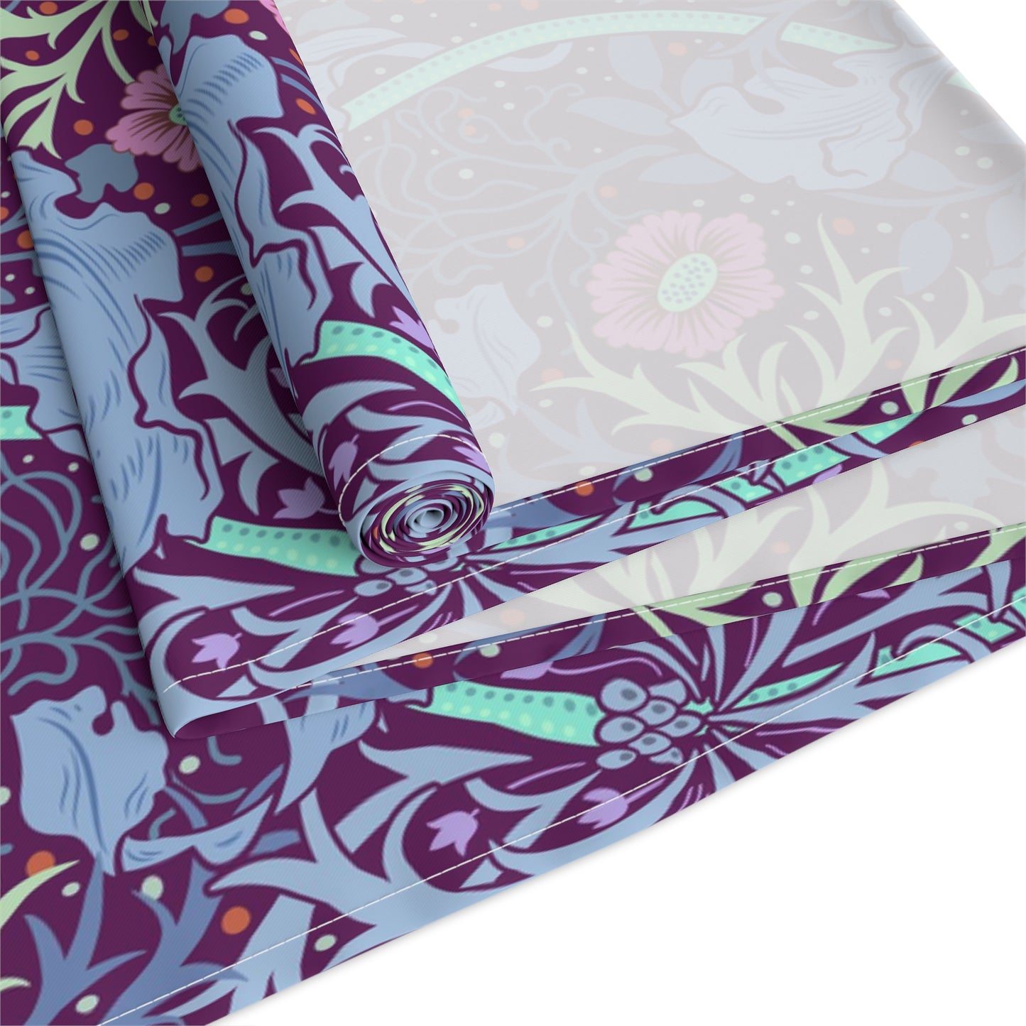 A multicolored table runner with a floral William Morris & Co pattern in pink and green on a blue background, displayed on a table with dishes and cutlery.