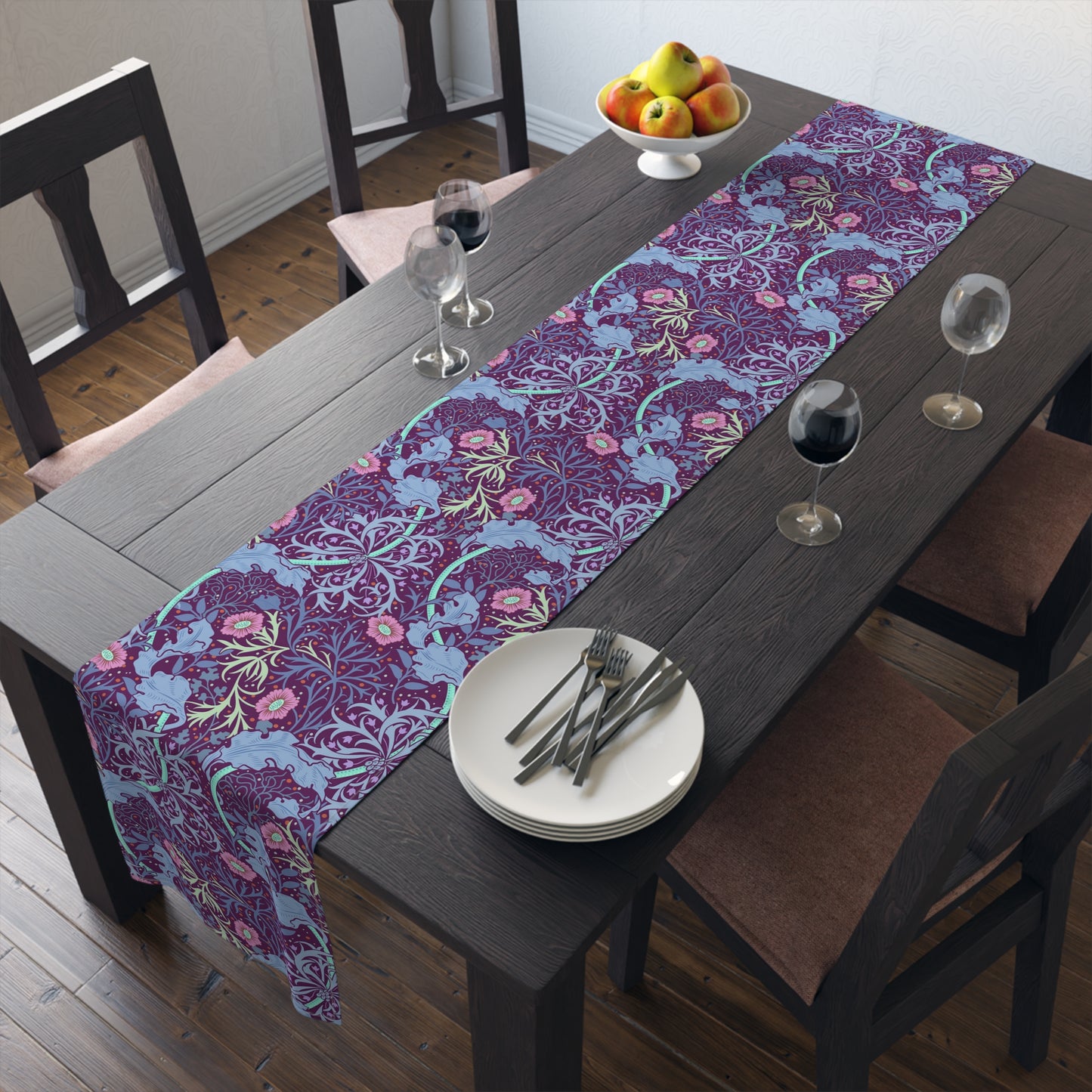 A multicolored table runner with a floral William Morris & Co pattern in pink and green on a blue background, displayed on a table with dishes and cutlery.
