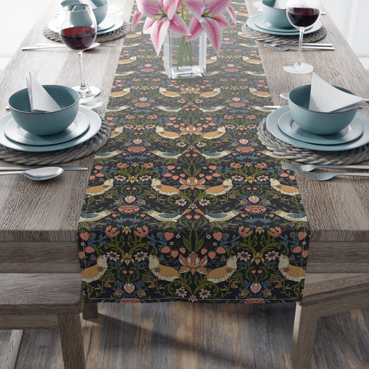 A table runner with a floral pattern in shades of black, green, and brown, laid out on a dining table with place settings and decorative elements in the background.