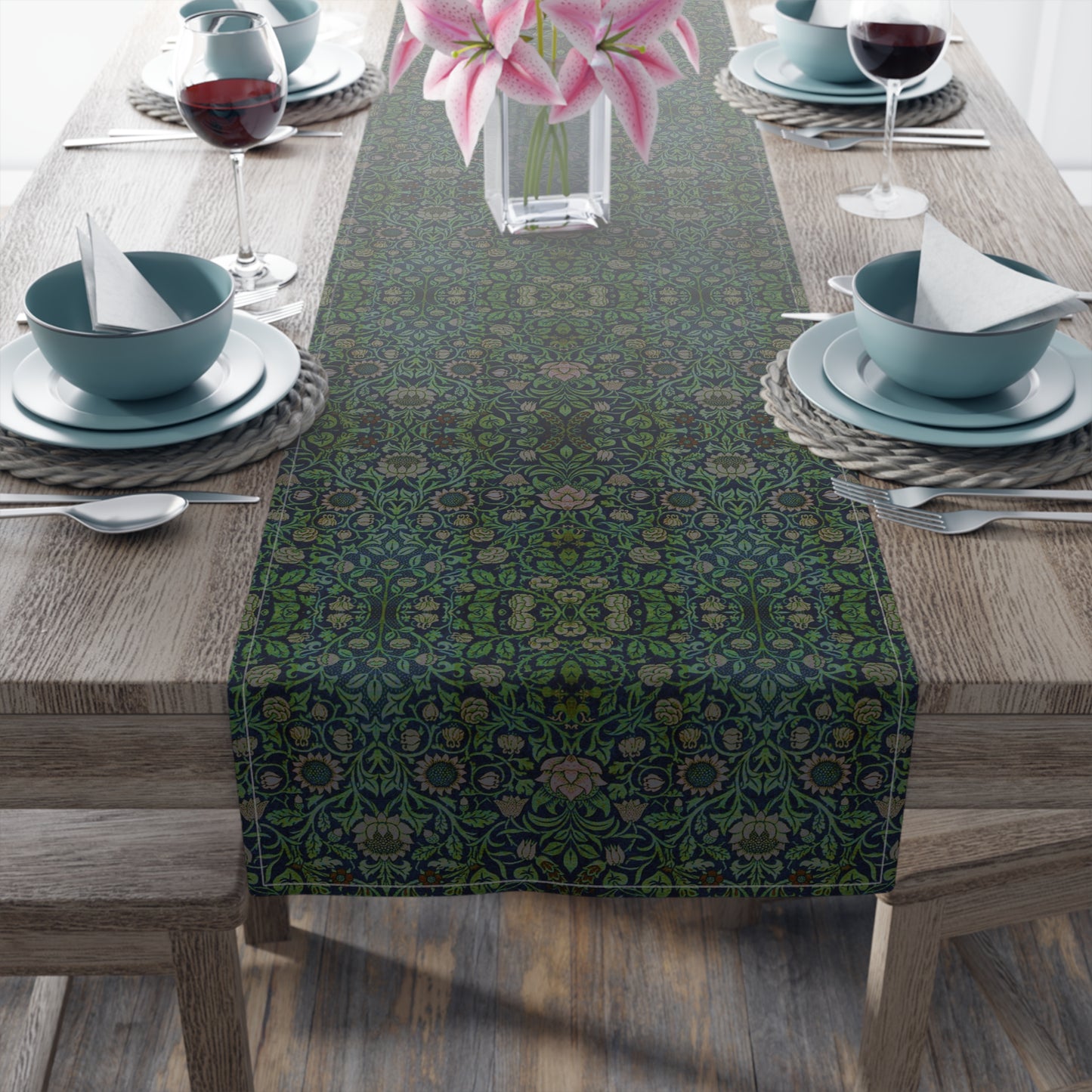 A green floral patterned table runner inspired by William Morris, laid out on a wooden dining table with plates and cutlery set on top.