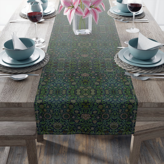 A green floral patterned table runner inspired by William Morris, laid out on a wooden dining table with plates and cutlery set on top.