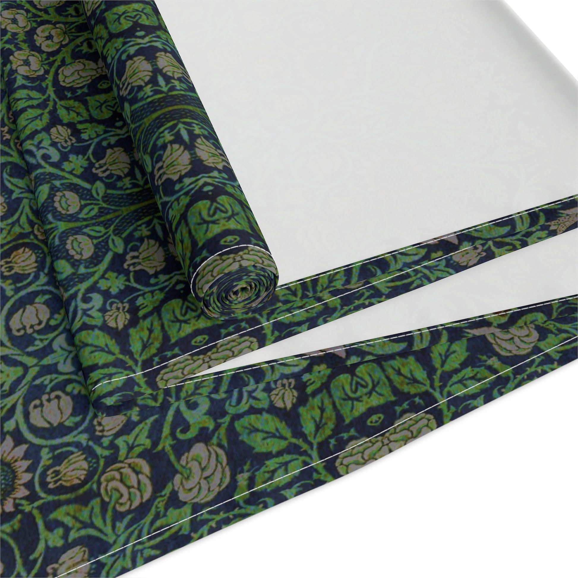 A green floral patterned table runner inspired by William Morris, laid out on a wooden dining table with plates and cutlery set on top.