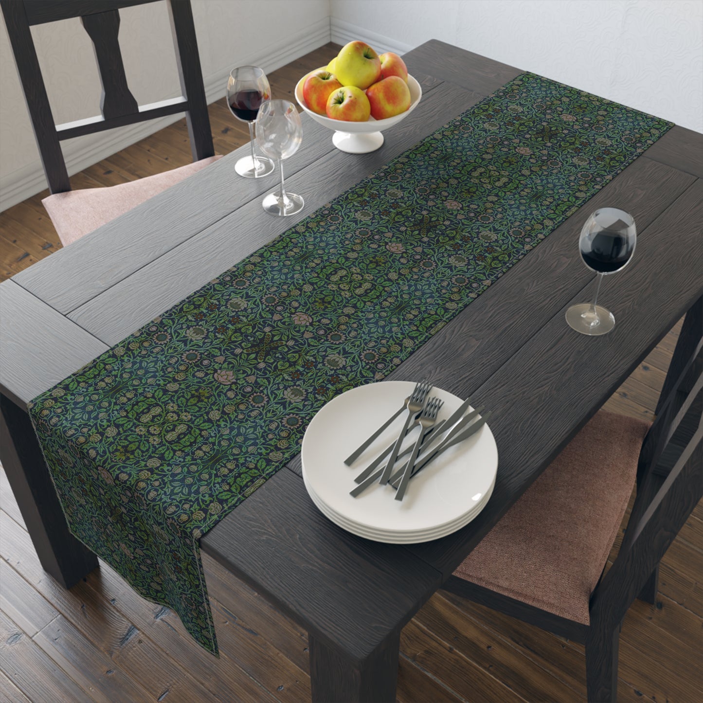 A green floral patterned table runner inspired by William Morris, laid out on a wooden dining table with plates and cutlery set on top.