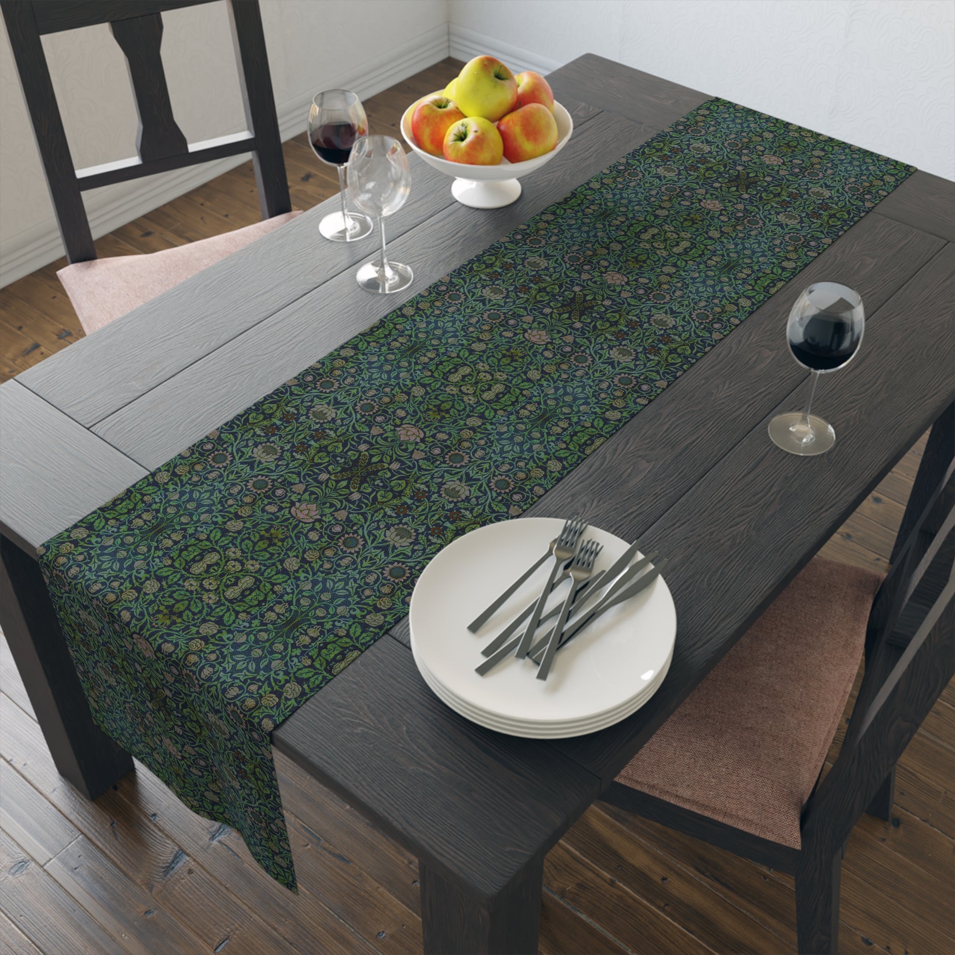 A green floral patterned table runner inspired by William Morris, laid out on a wooden dining table with plates and cutlery set on top.
