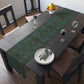 A green floral patterned table runner inspired by William Morris, laid out on a wooden dining table with plates and cutlery set on top.