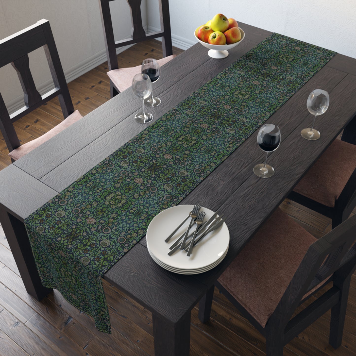 A green floral patterned table runner inspired by William Morris, laid out on a wooden dining table with plates and cutlery set on top.