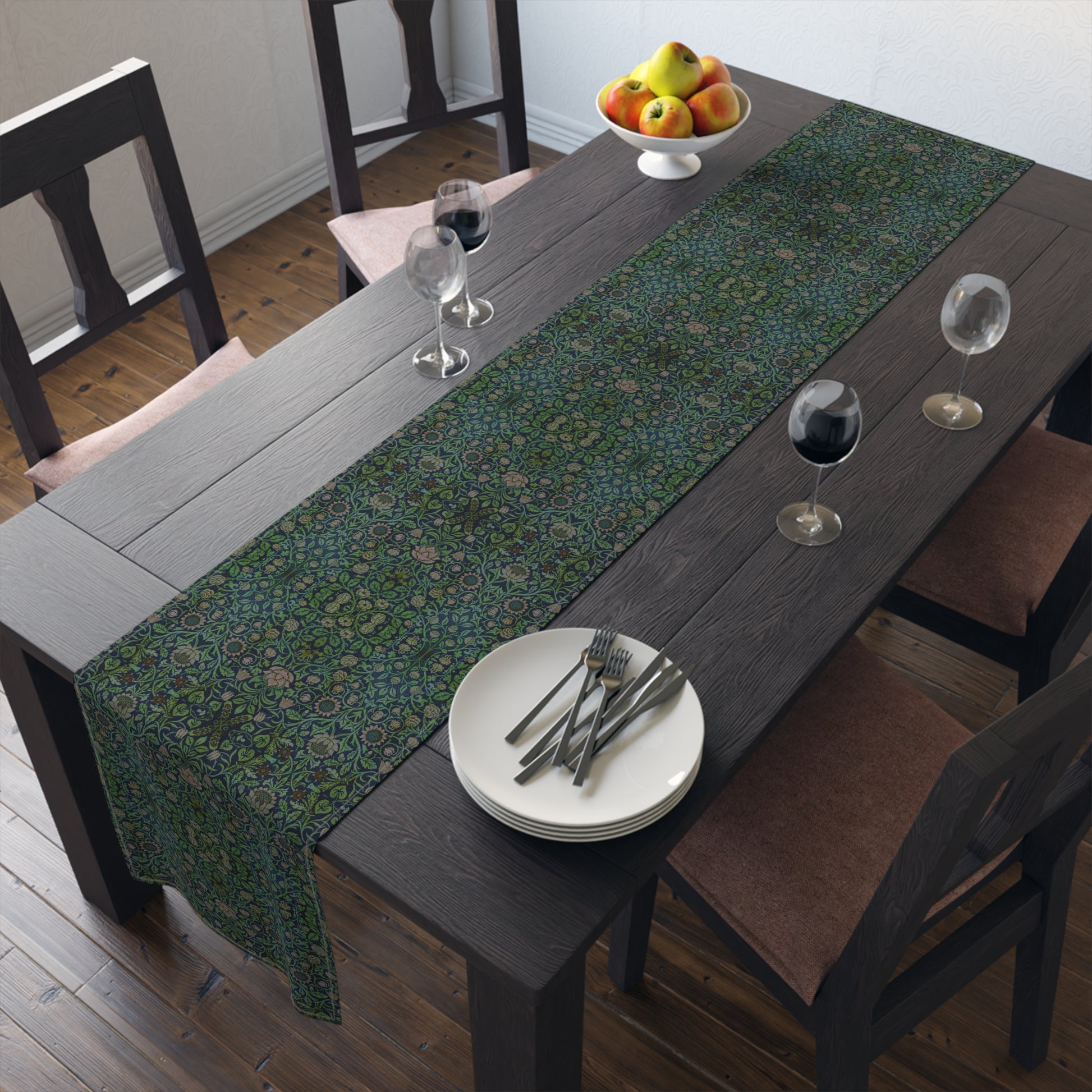 A green floral patterned table runner inspired by William Morris, laid out on a wooden dining table with plates and cutlery set on top.