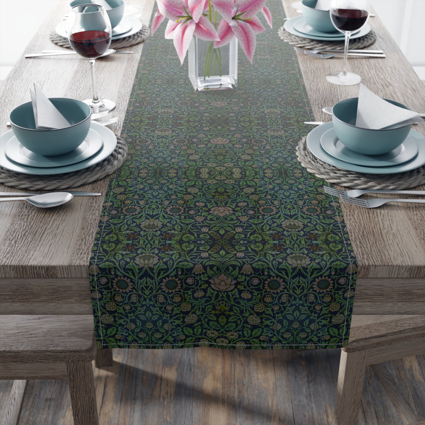 A green floral patterned table runner inspired by William Morris, laid out on a wooden dining table with plates and cutlery set on top.
