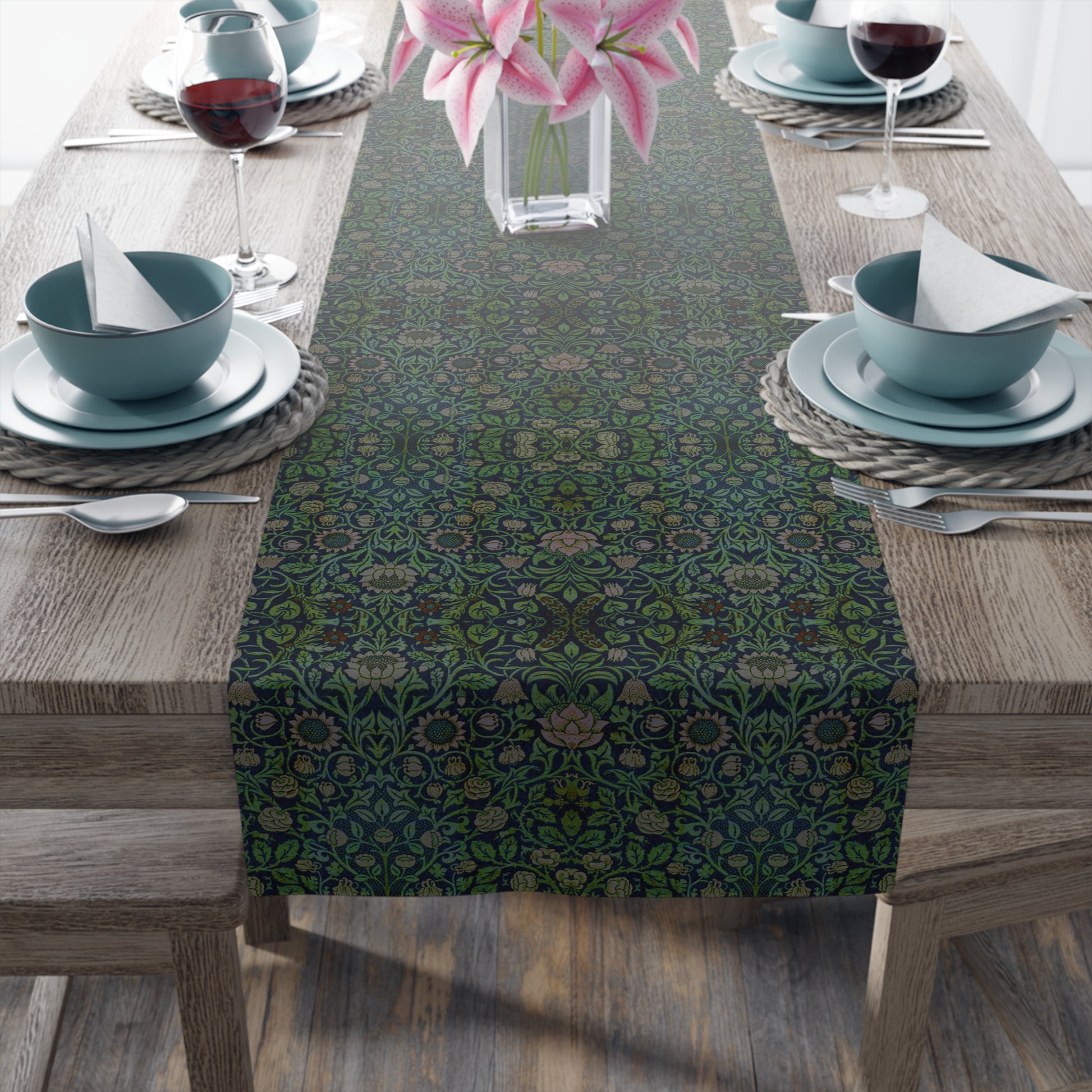 A green floral patterned table runner inspired by William Morris, laid out on a wooden dining table with plates and cutlery set on top.