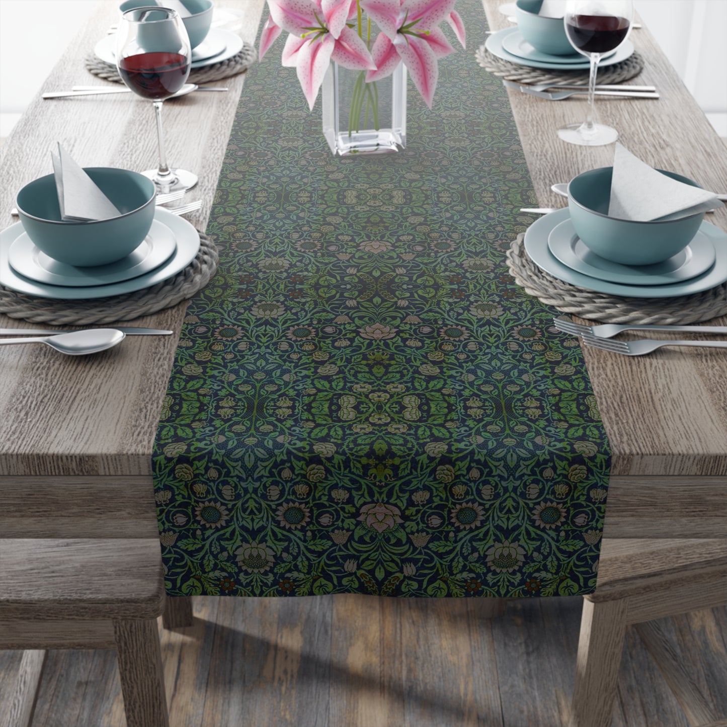 A green floral patterned table runner inspired by William Morris, laid out on a wooden dining table with plates and cutlery set on top.