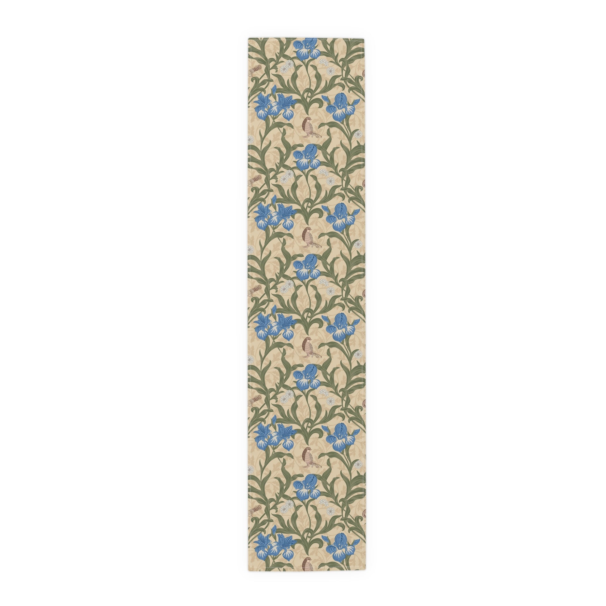 A table runner with a Victorian floral design in blue and green on a beige background, laid out on a dining table with place settings and decorative flowers.