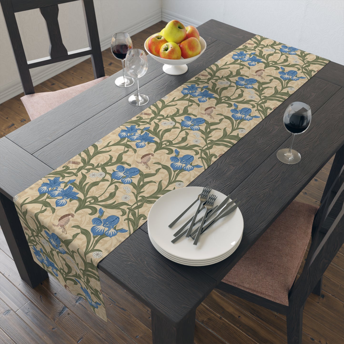 A table runner with a Victorian floral design in blue and green on a beige background, laid out on a dining table with place settings and decorative flowers.