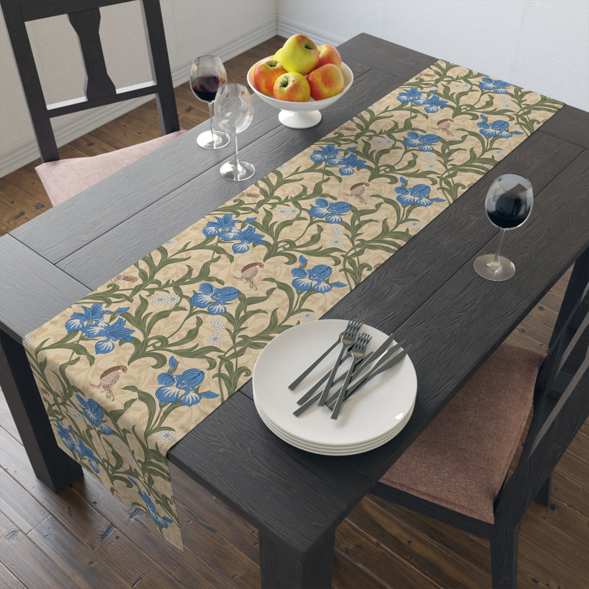A table runner with a Victorian floral design in blue and green on a beige background, laid out on a dining table with place settings and decorative flowers.