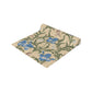 A table runner with a Victorian floral design in blue and green on a beige background, laid out on a dining table with place settings and decorative flowers.