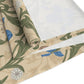 A table runner with a Victorian floral design in blue and green on a beige background, laid out on a dining table with place settings and decorative flowers.