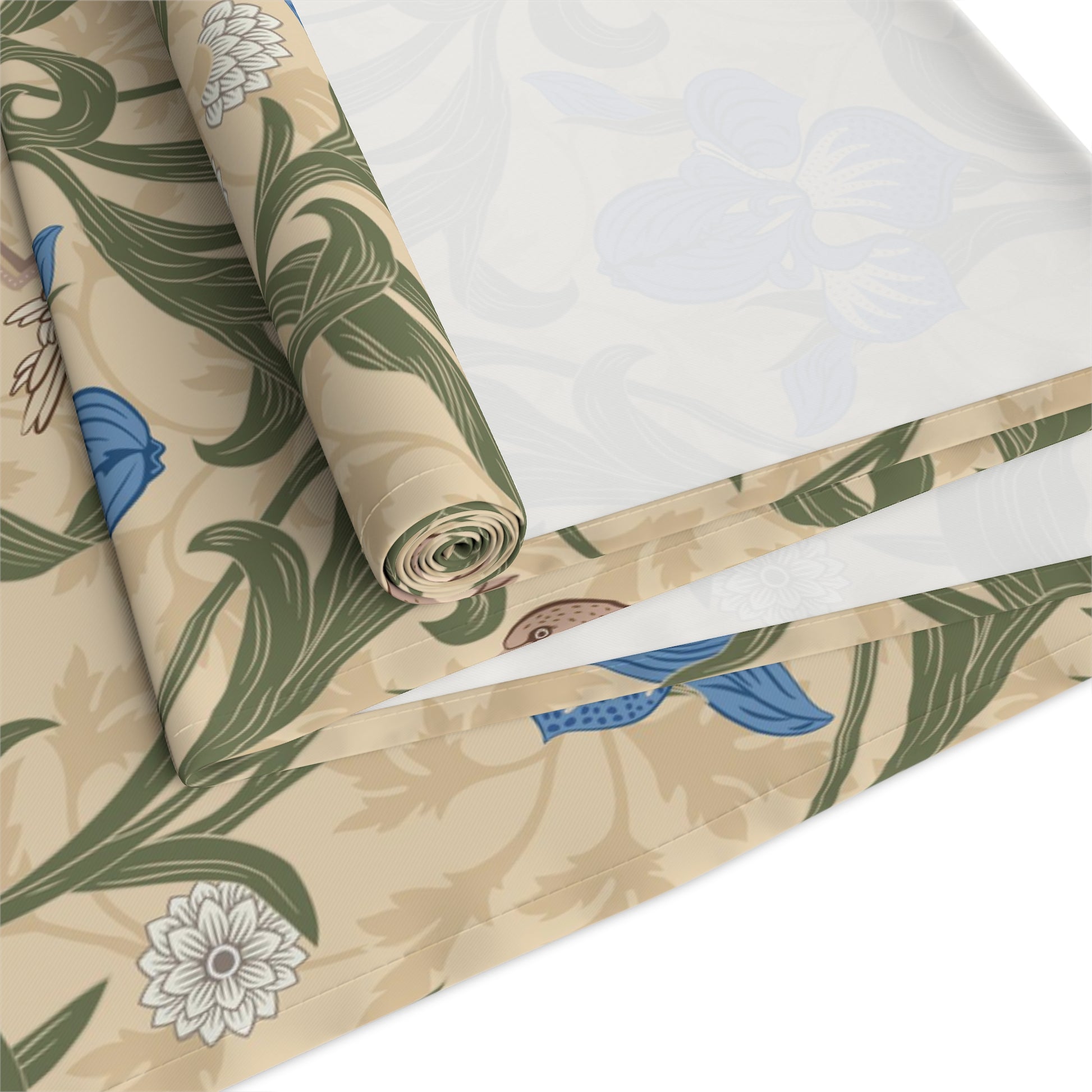 A table runner with a Victorian floral design in blue and green on a beige background, laid out on a dining table with place settings and decorative flowers.