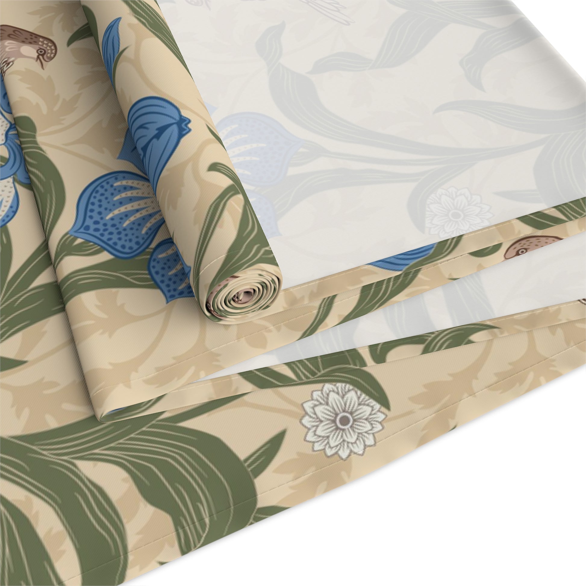 A table runner with a Victorian floral design in blue and green on a beige background, laid out on a dining table with place settings and decorative flowers.