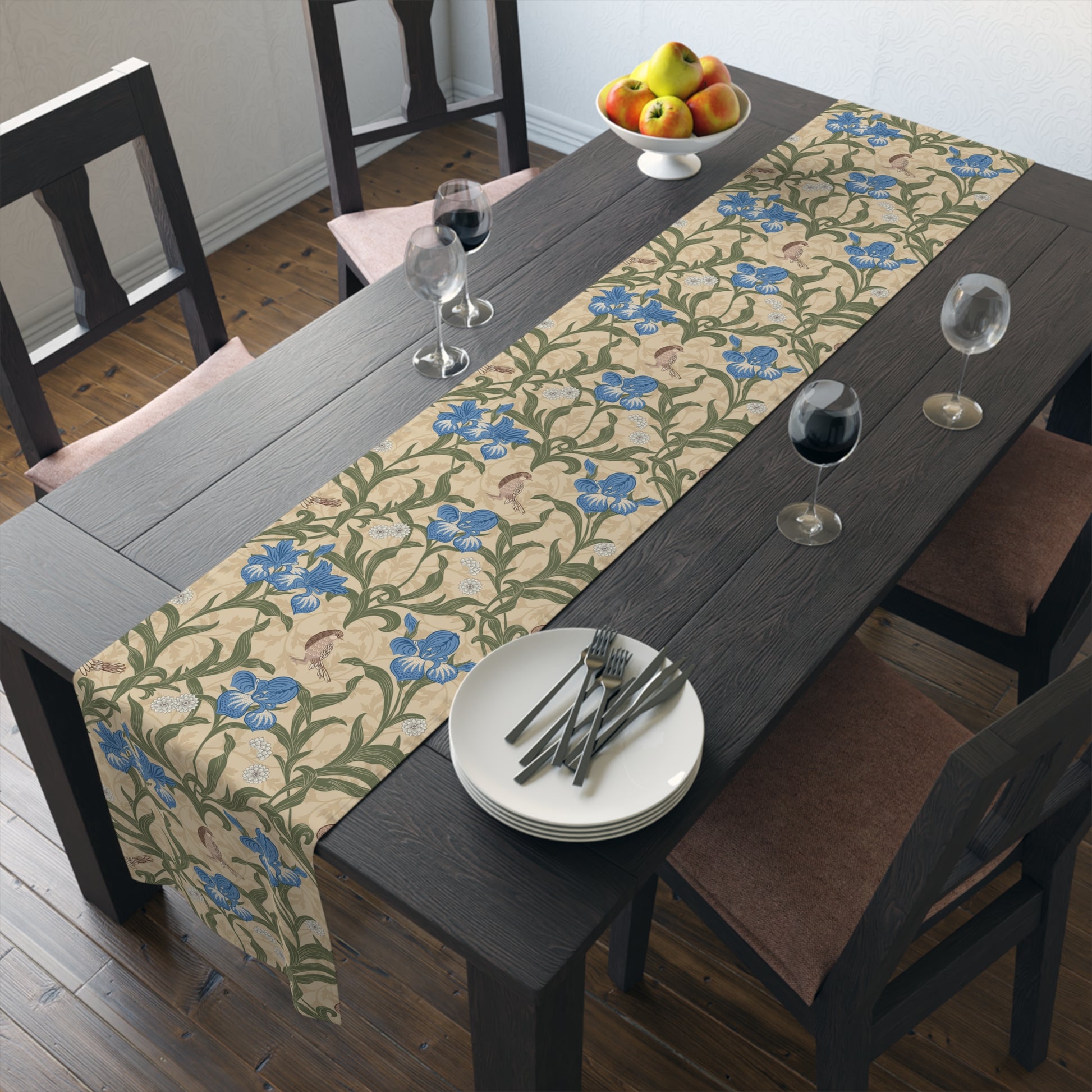 A table runner with a Victorian floral design in blue and green on a beige background, laid out on a dining table with place settings and decorative flowers.