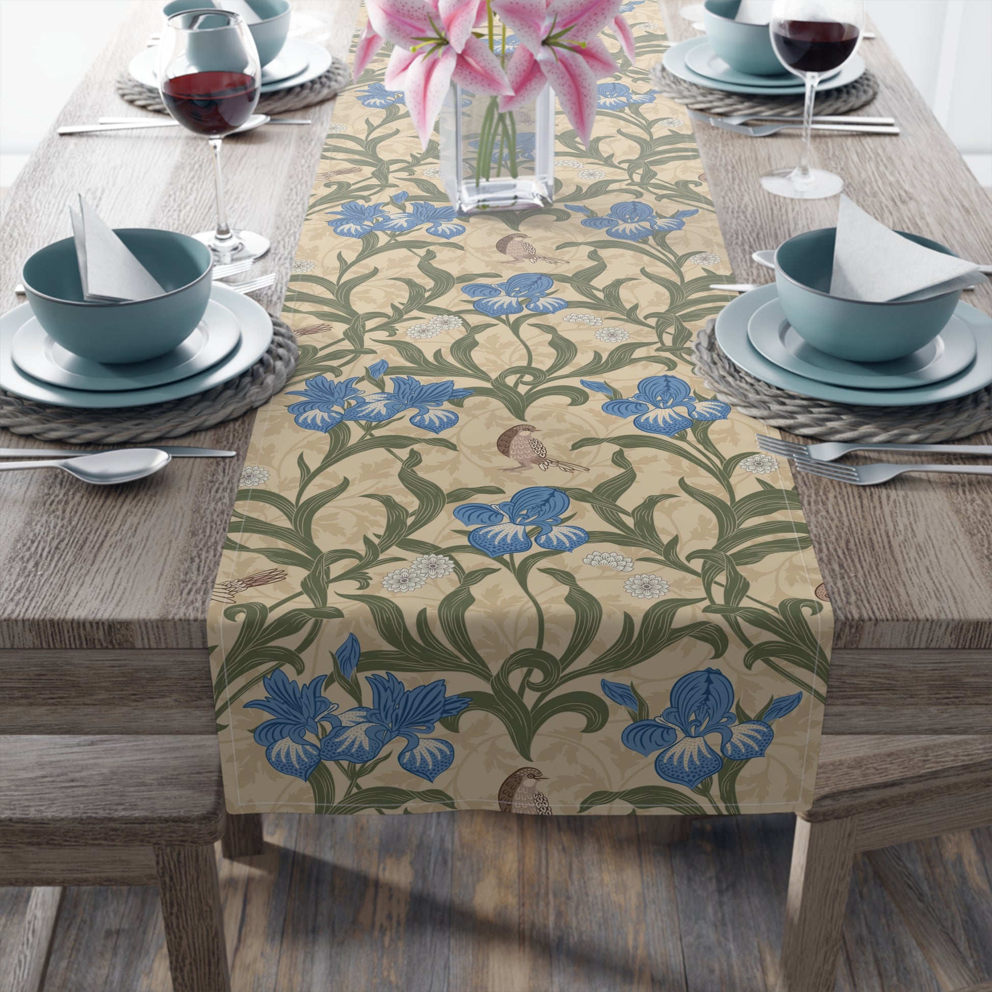 A table runner with a Victorian floral design in blue and green on a beige background, laid out on a dining table with place settings and decorative flowers.