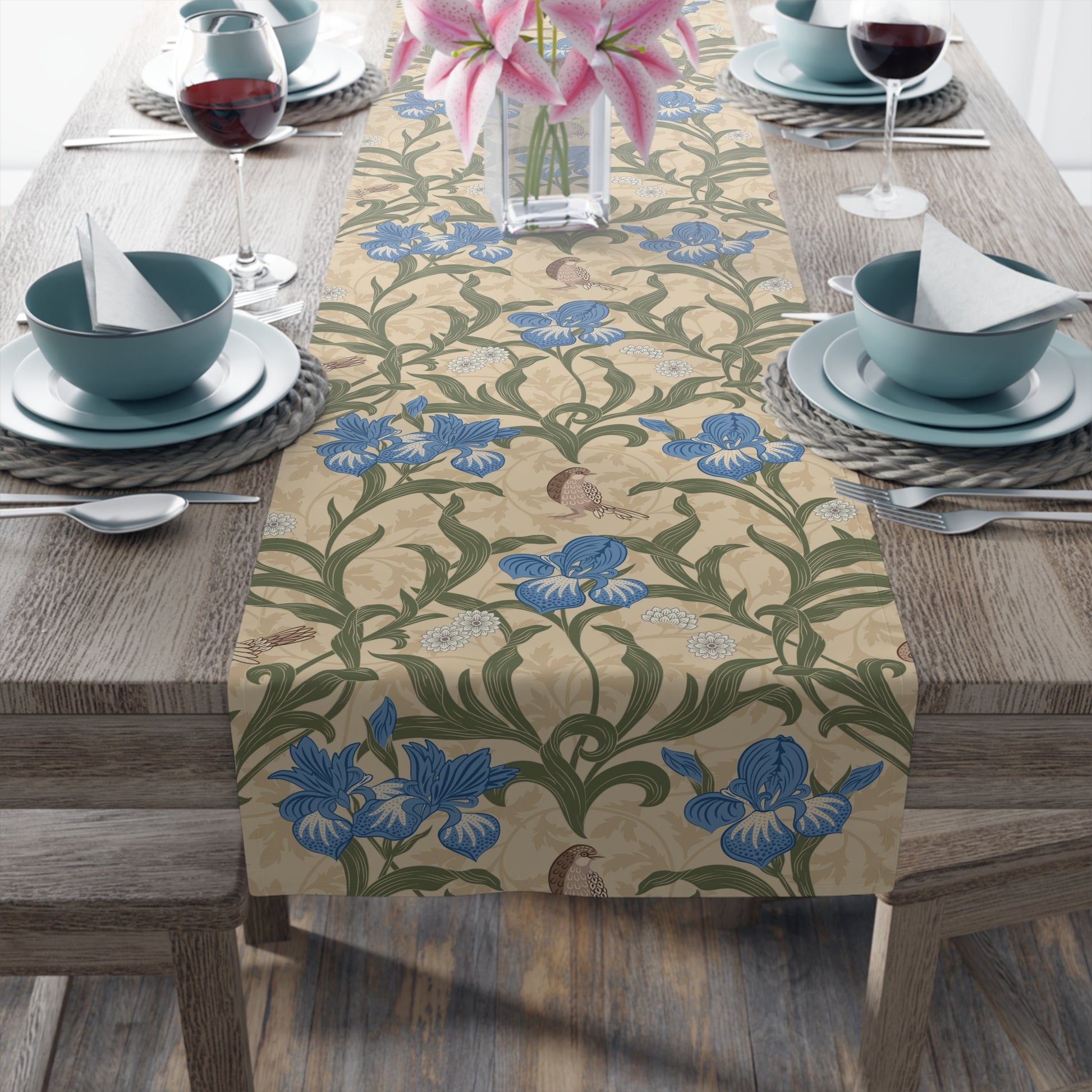 A table runner with a Victorian floral design in blue and green on a beige background, laid out on a dining table with place settings and decorative flowers.