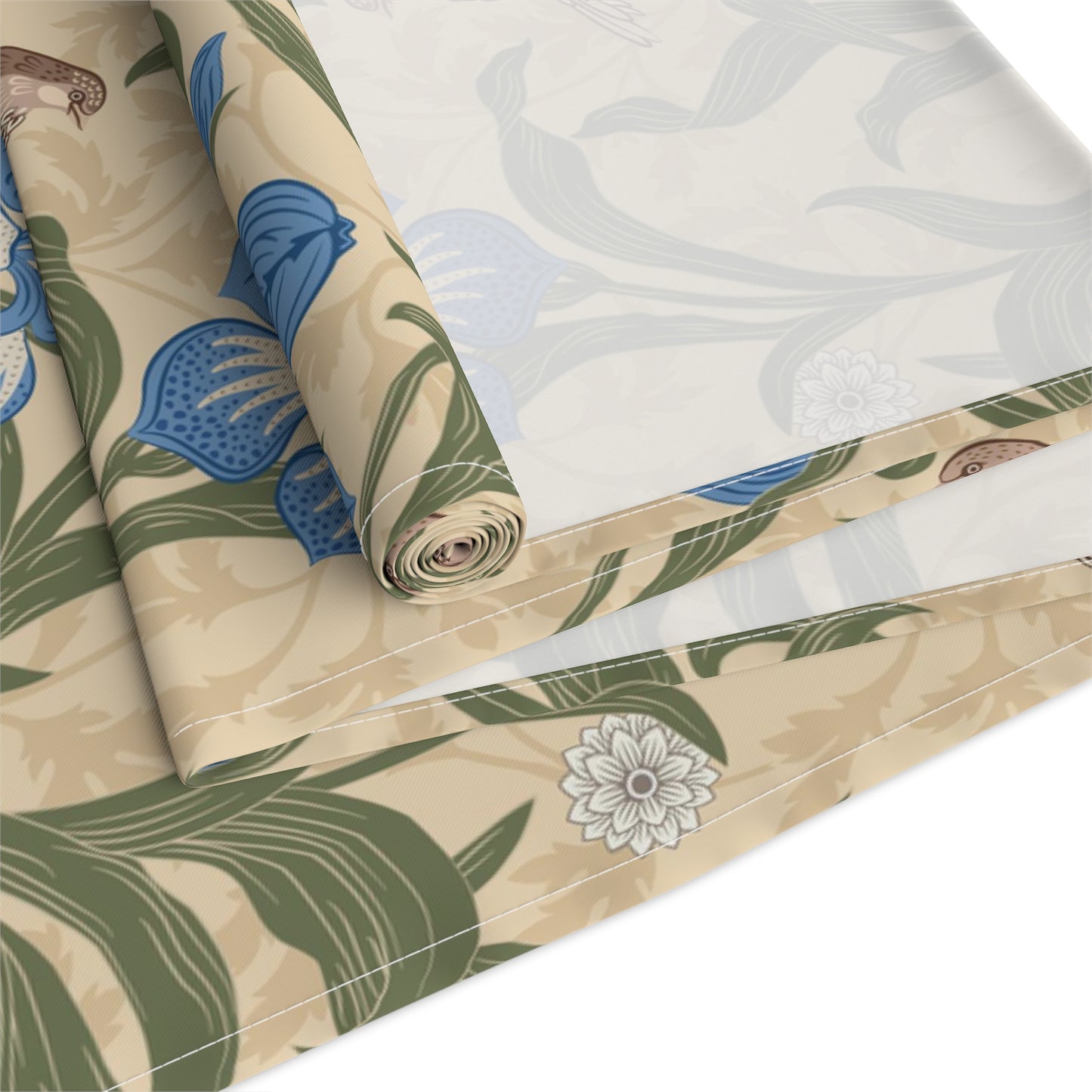 A table runner with a Victorian floral design in blue and green on a beige background, laid out on a dining table with place settings and decorative flowers.