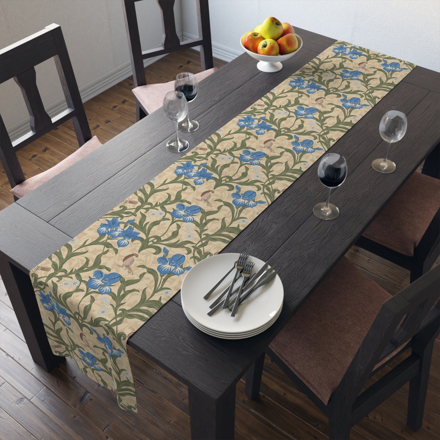 A table runner with a Victorian floral design in blue and green on a beige background, laid out on a dining table with place settings and decorative flowers.
