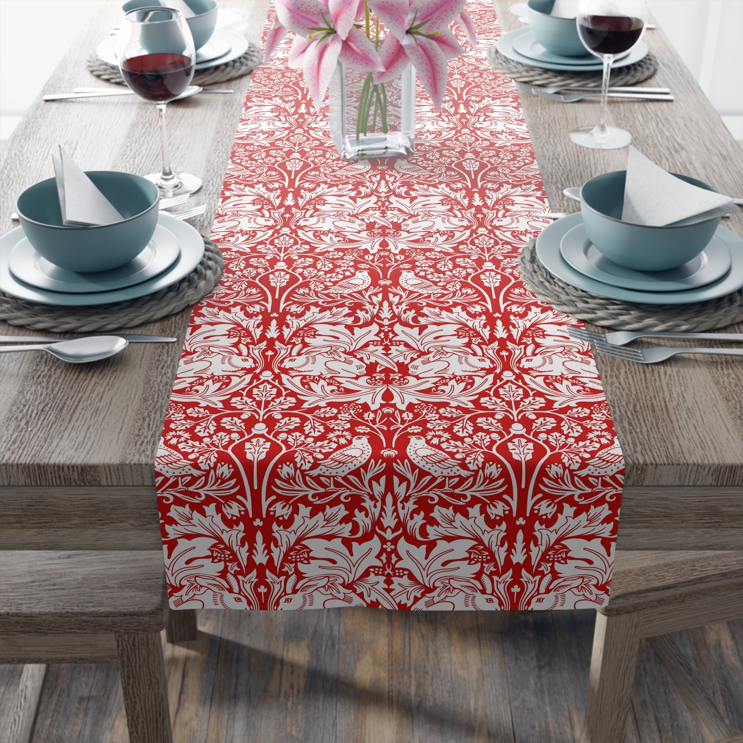 Dining table set with a red and white patterned table runner, blue bowls, and pink flowers.