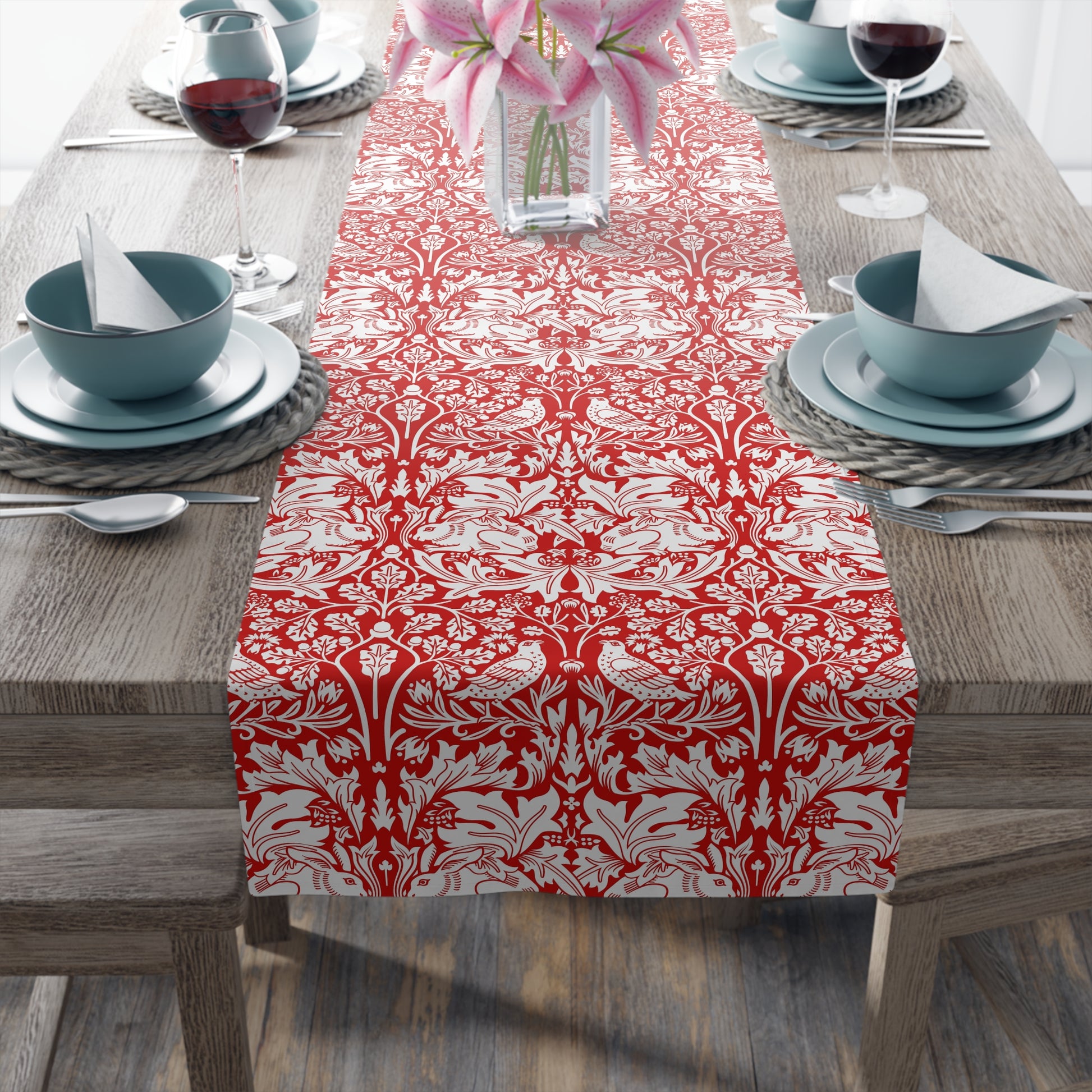 Dining table set with a red and white patterned table runner, blue bowls, and pink flowers.