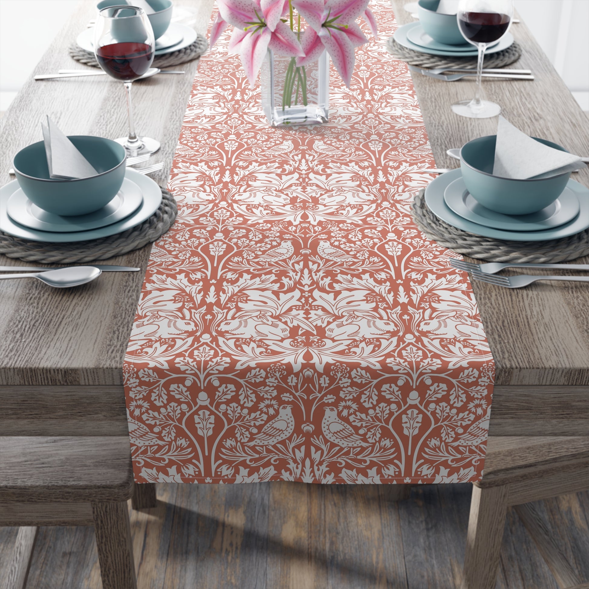 Dining table set with a patterned table runner, blue bowls, and pink flowers.