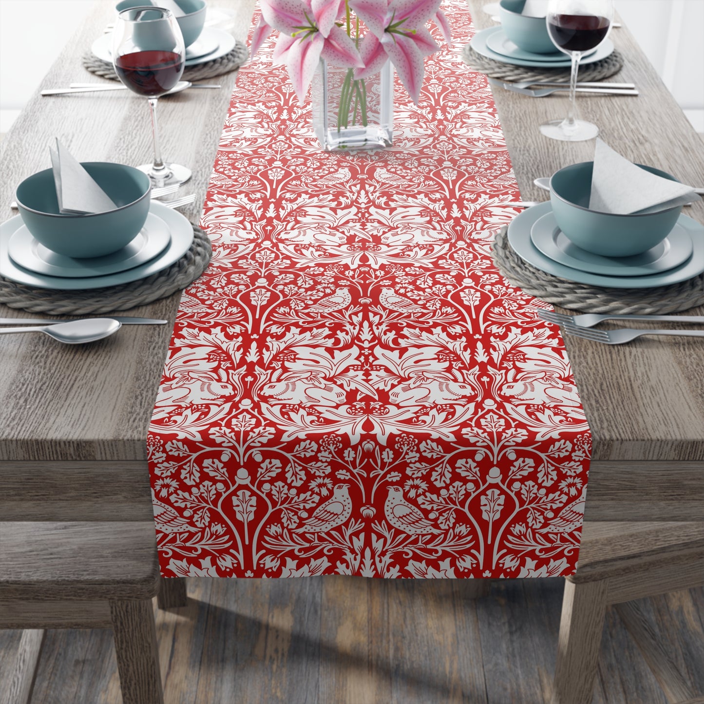 Dining table set with a red and white patterned table runner, blue bowls, and pink flowers.