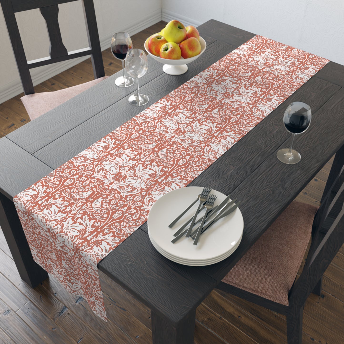Dining table with a floral patterned table runner, plates, forks, and a bowl of fruit.