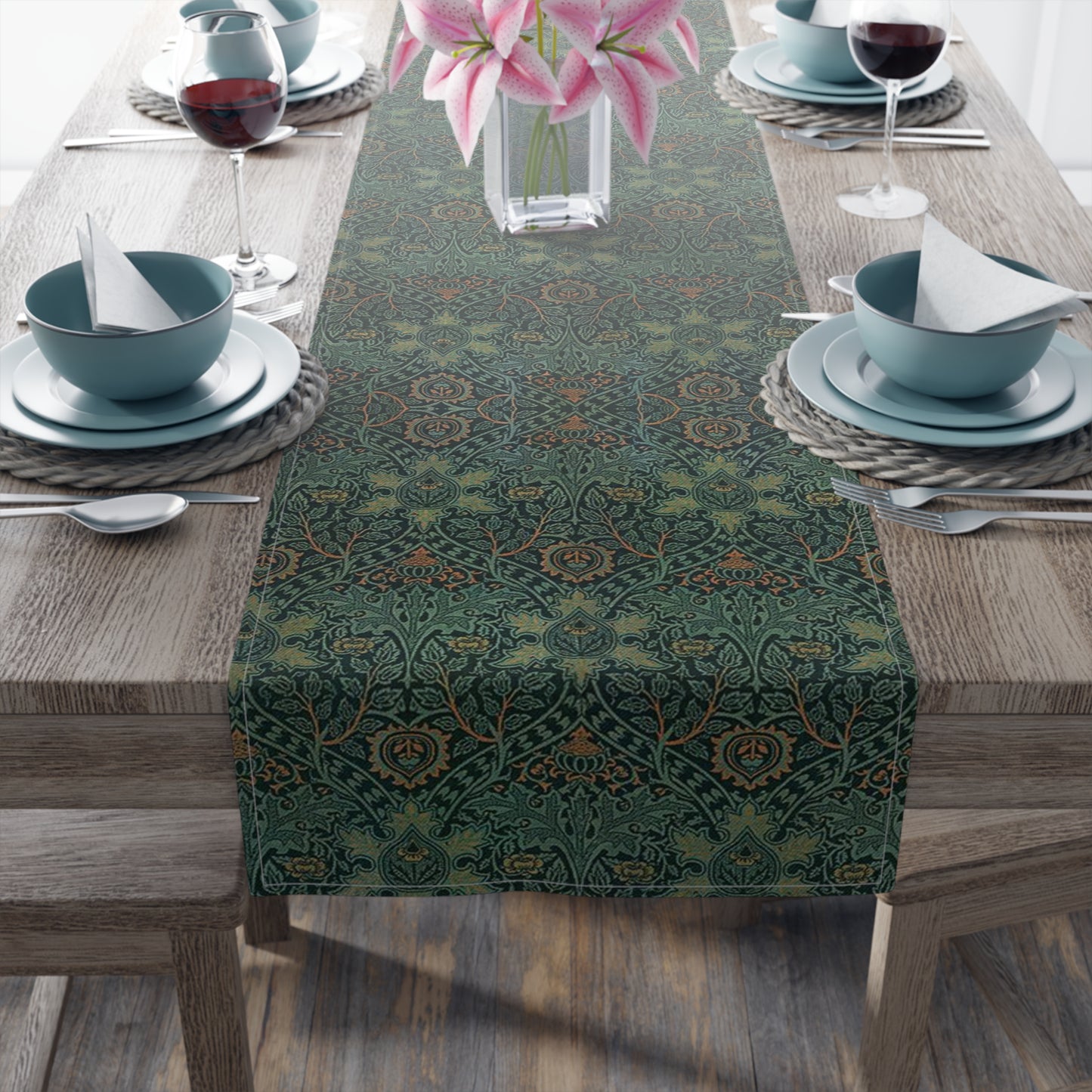 A green table runner with a floral pattern inspired by William Morris, displayed on a dining table with dishes and cutlery.