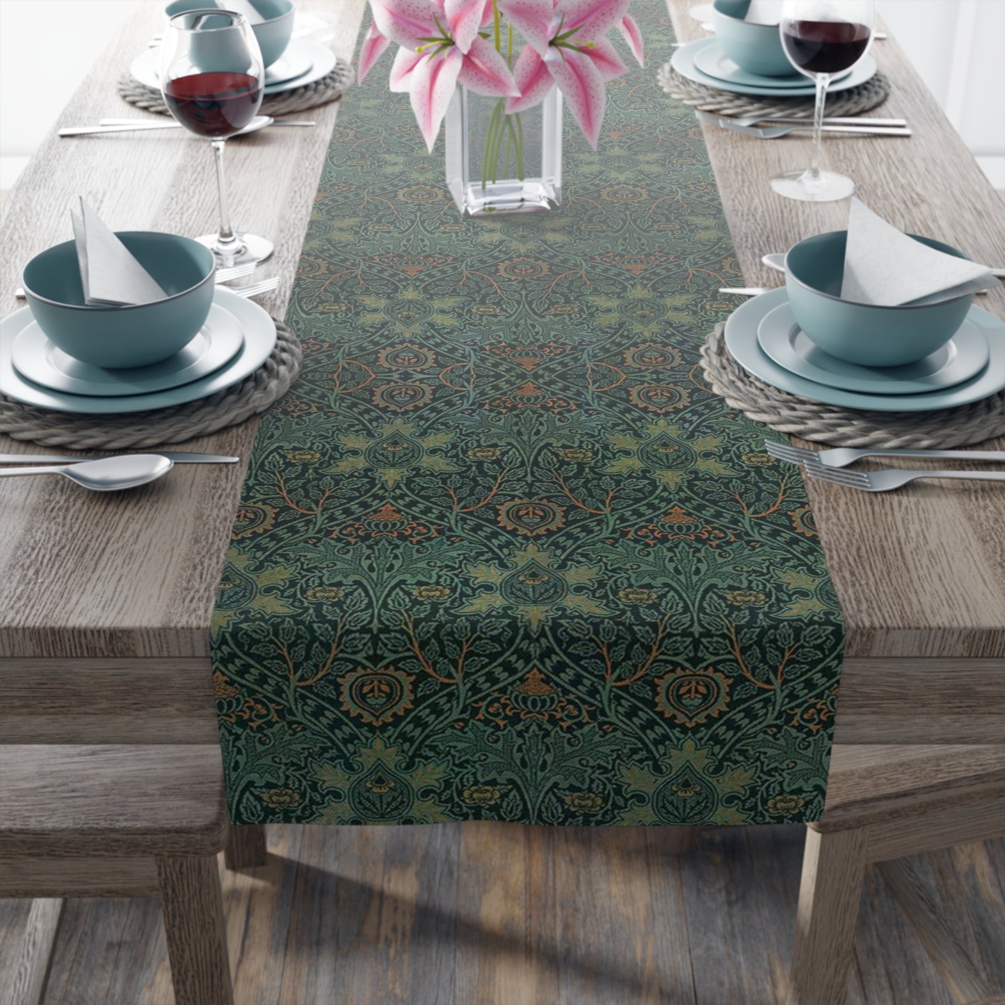 A green table runner with a floral pattern inspired by William Morris, displayed on a dining table with dishes and cutlery.