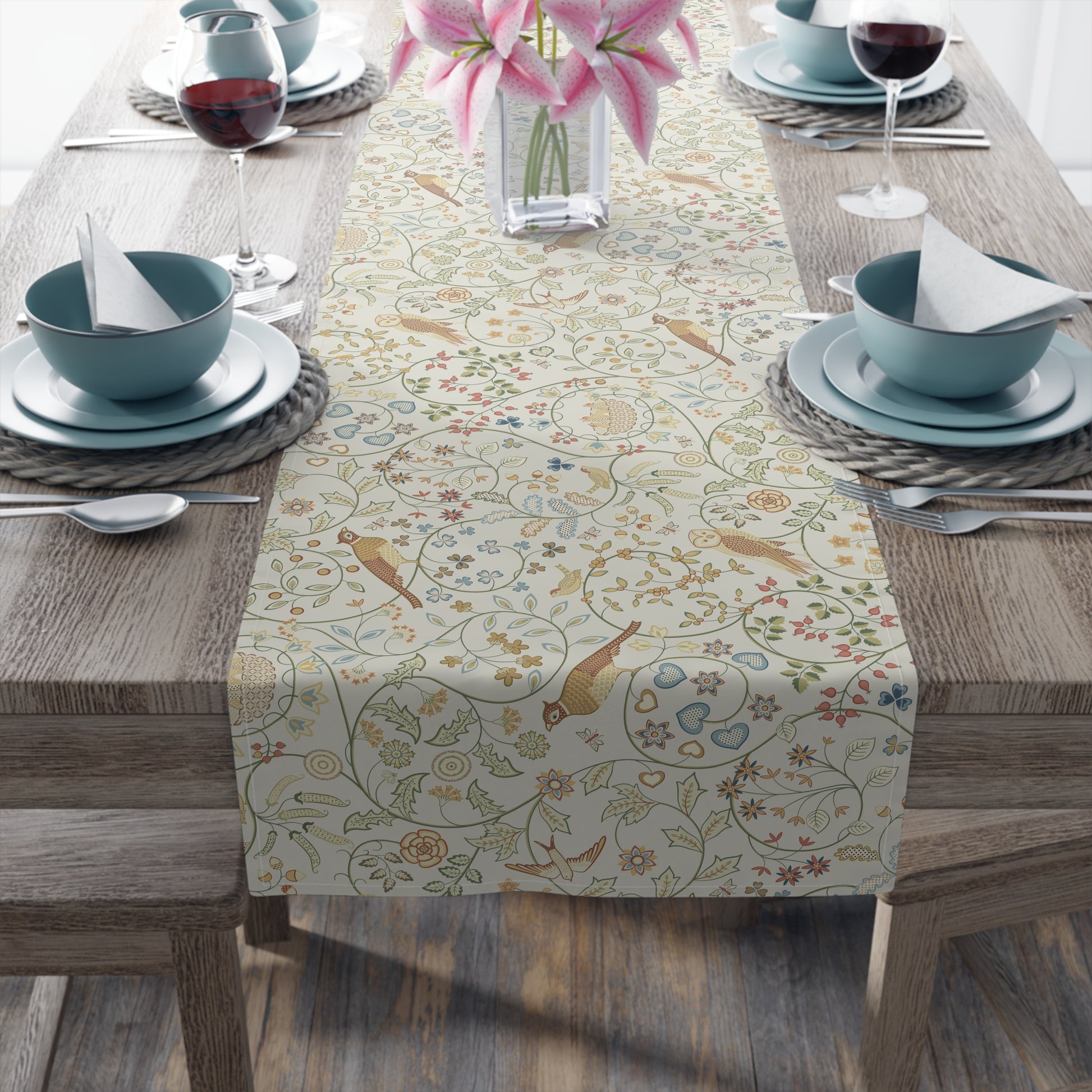 Decorative table runner with floral and bird pattern on a wooden table with place settings.