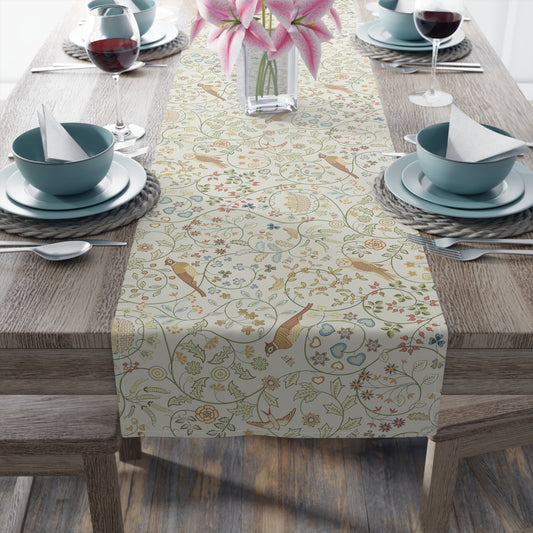 Decorative table runner with floral and bird pattern on a wooden table with place settings.