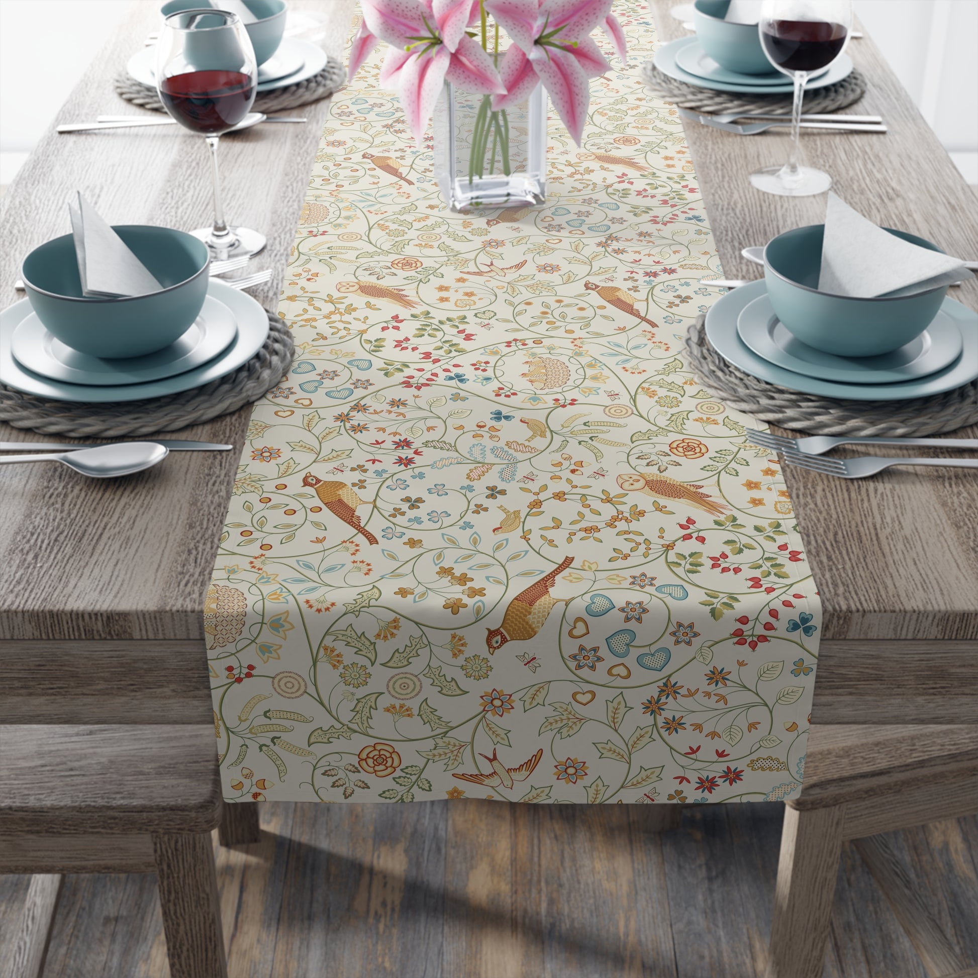 Decorative table runner with floral and bird pattern on a wooden table with dinnerware.