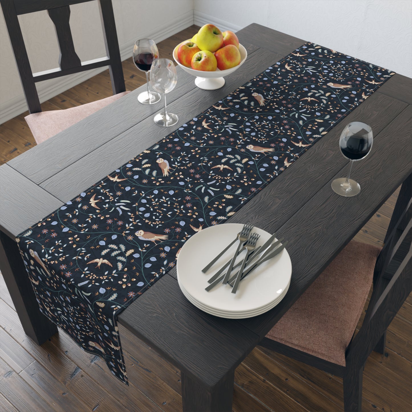 Table runner with floral pattern on a wooden table with plates, forks, and wine glasses.
