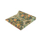 A table runner with a floral pattern inspired by William Morris, displayed on a dining table set with dishes and glasses.