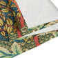 A table runner with a floral pattern inspired by William Morris, displayed on a dining table set with dishes and glasses.