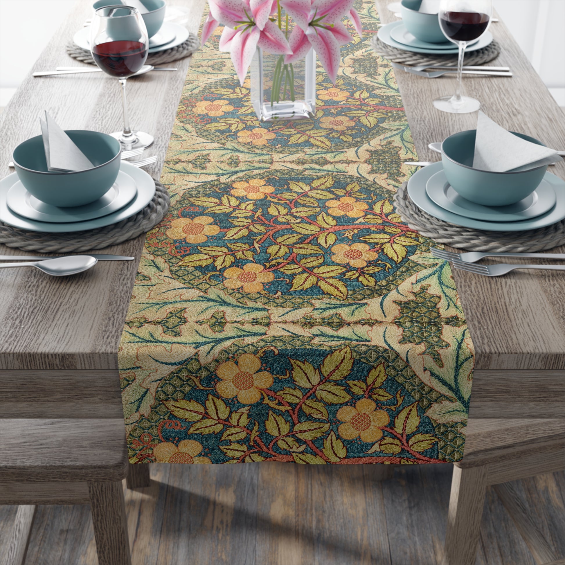 A table runner with a floral pattern inspired by William Morris, displayed on a dining table set with dishes and glasses.