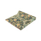 A table runner with a floral pattern inspired by William Morris, displayed on a dining table set with dishes and glasses.