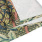 A table runner with a floral pattern inspired by William Morris, displayed on a dining table set with dishes and glasses.