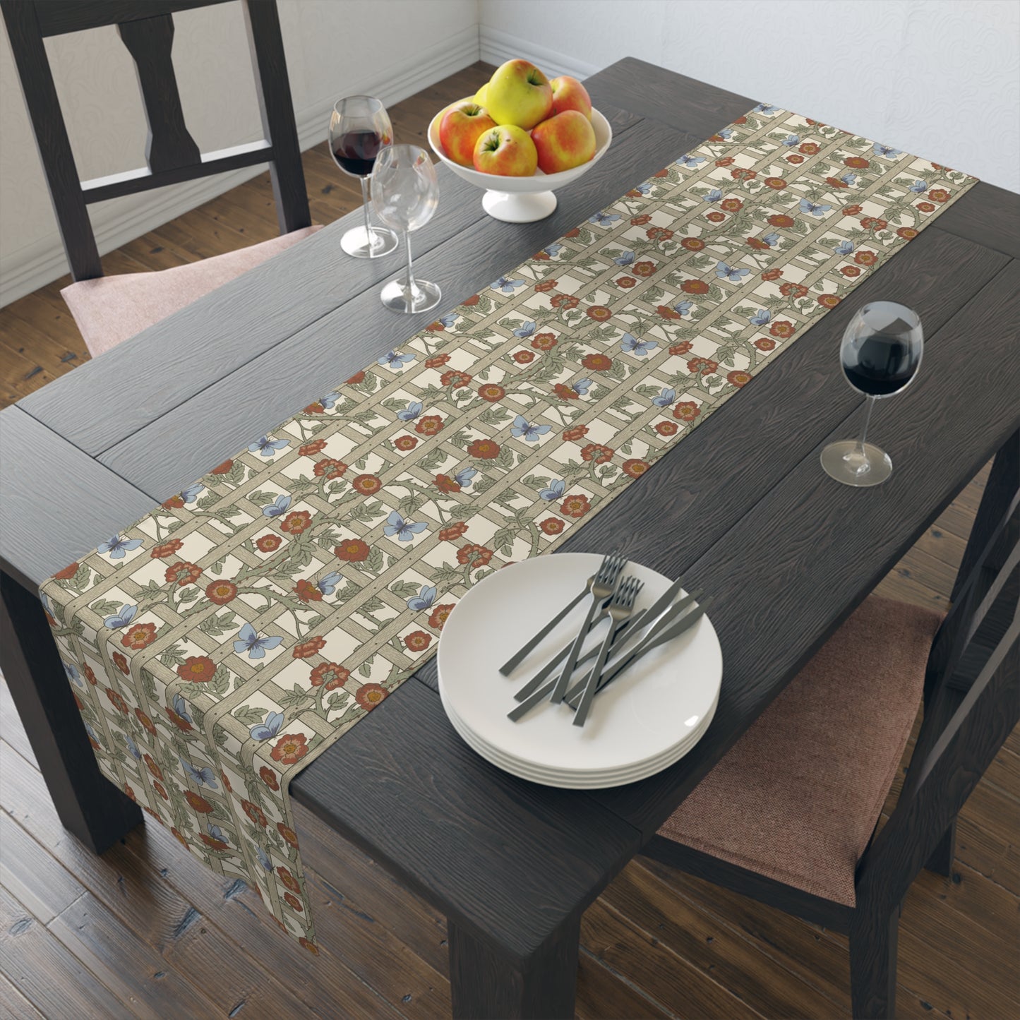 Dining table with floral-patterned table runner, plates, forks, and a bowl of fruit.