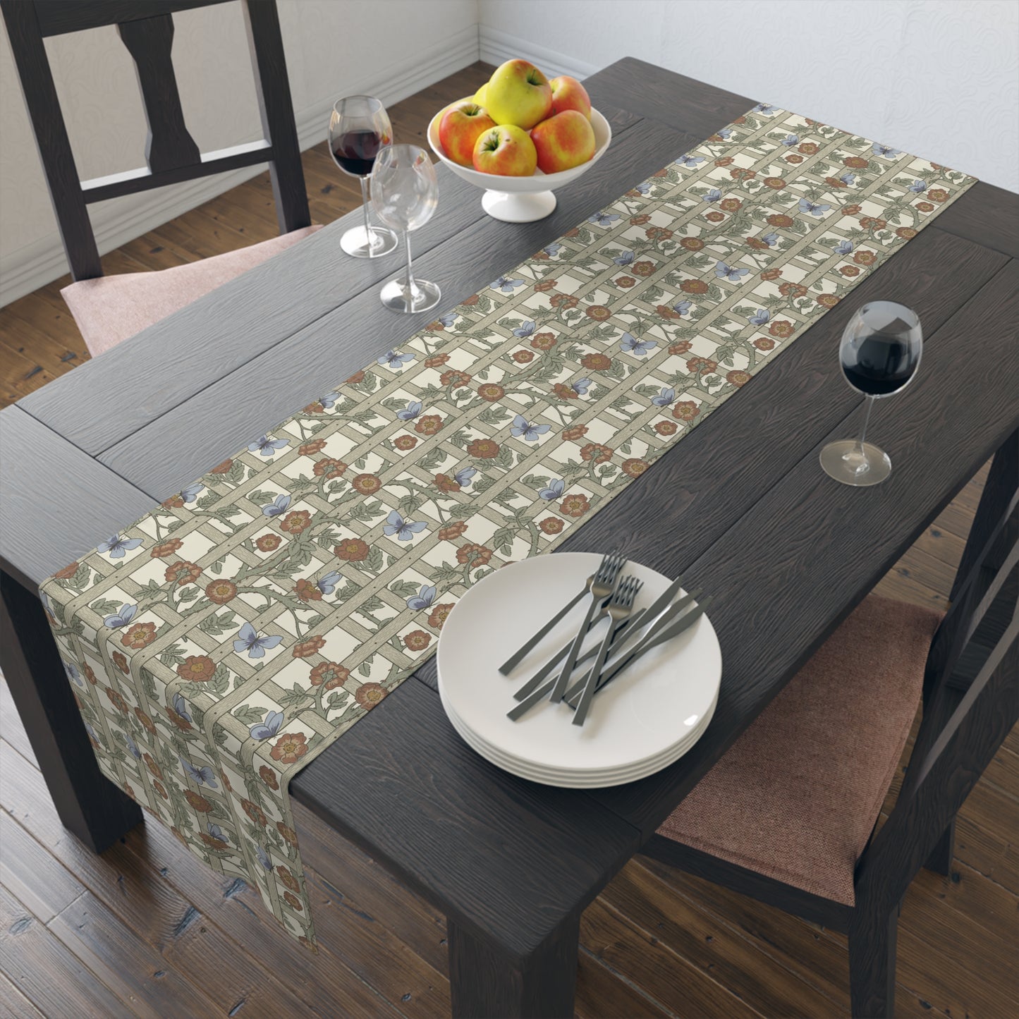 Dining table with a patterned table runner, plates, forks, and a bowl of fruit.
