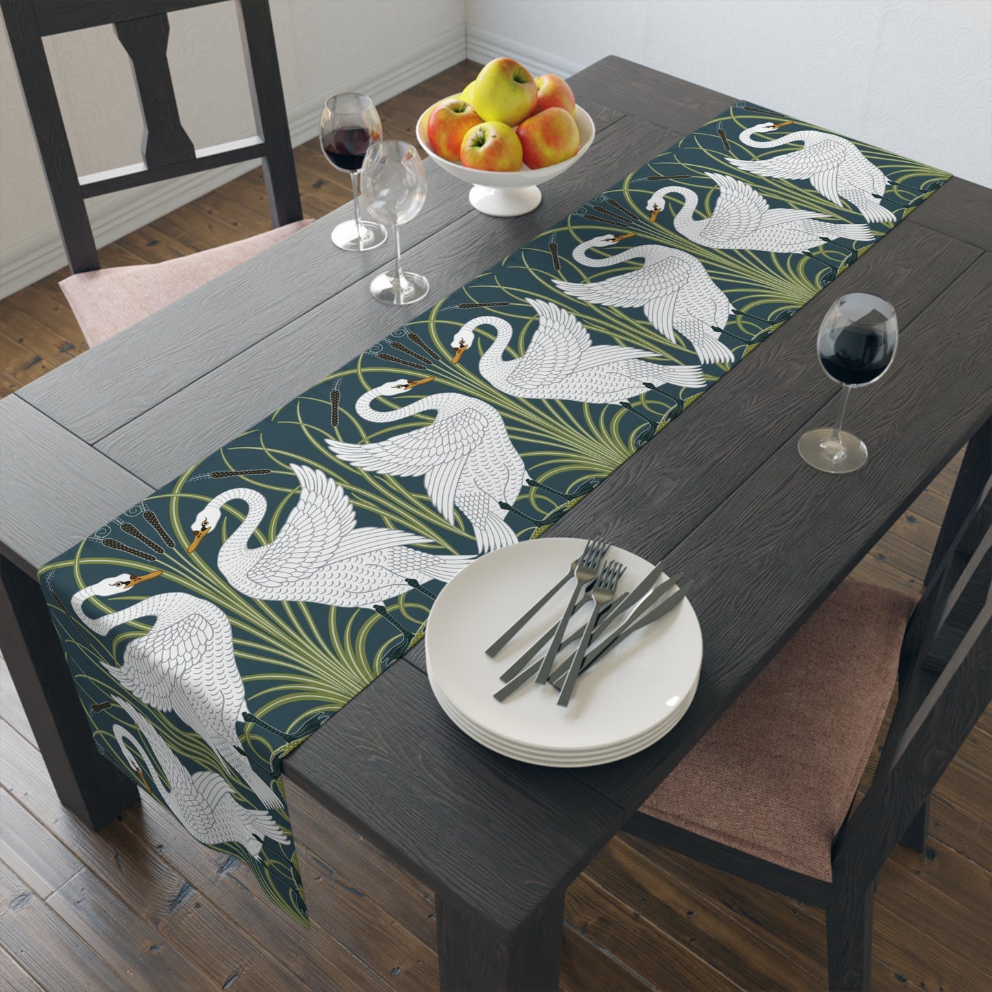 Dining table with a swan patterned table runner, plates, cutlery, and fruit.