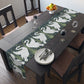 Dining table with a swan patterned table runner, plates, and glasses.
